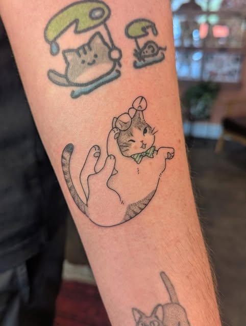 Fine-line cat tattoo wearing a tiny party hat