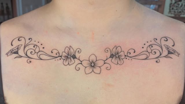 Symmetrical floral line tattoo across the upper chest